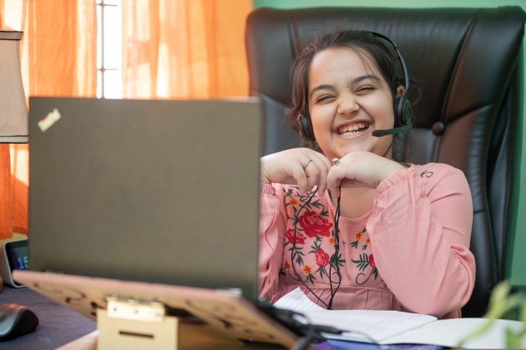 Smiling young girl with headset on a video call, studying online at home.