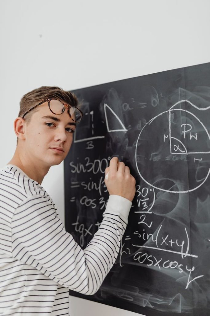 Teenager writing mathematical equations on blackboard, focused learning.