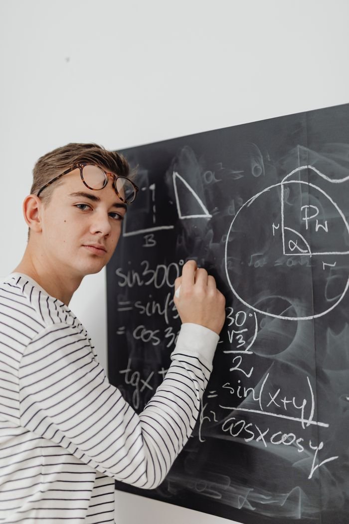 Teenager writing mathematical equations on blackboard, focused learning.